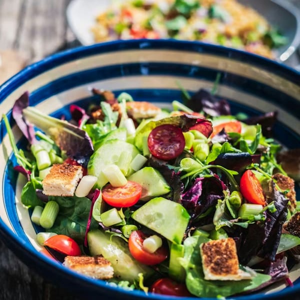 A vibrant garden salad with mixed greens, cherry tomatoes, cucumbers, and croutons in a blue and white striped bowl.