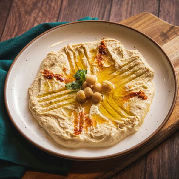 Creamy hummus drizzled with olive oil, garnished with chickpeas, paprika, and cilantro on a white plate.