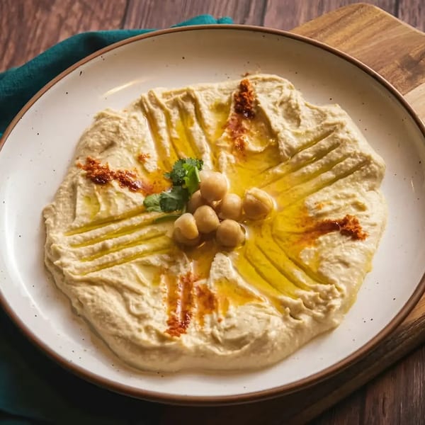 Creamy hummus drizzled with olive oil, garnished with chickpeas, paprika, and cilantro on a white plate.